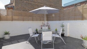 A patio with a table and chairs, a white umbrella, and potted plants.