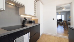 A modern kitchen with a black induction cooktop, a built-in oven, and a microwave. There is a wooden countertop, a knife block, and a toaster. The kitchen has white cabinets and a wooden floor.