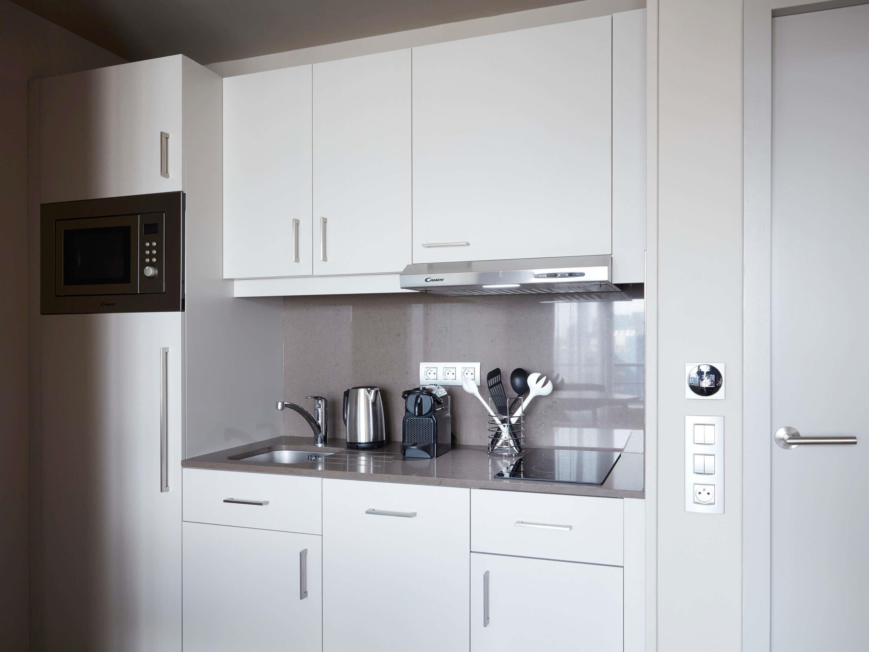 A compact kitchen with white cabinets, a built-in microwave, stainless steel appliances, and a countertop with a kettle and utensils.
