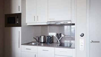 A compact kitchen with white cabinets, a built-in microwave, stainless steel appliances, and a countertop with a kettle and utensils.