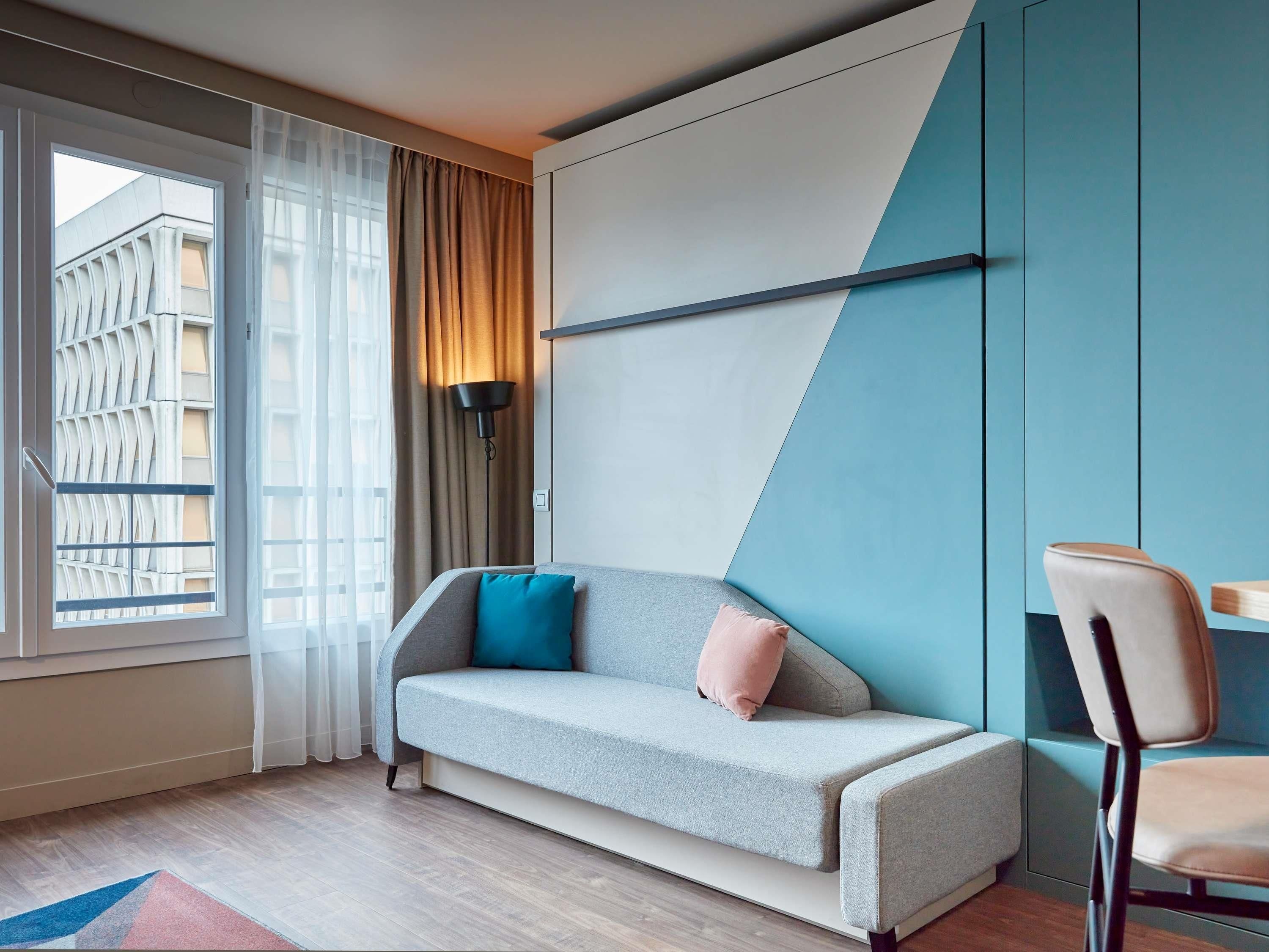 A modern room with a sofa, a chair, a lamp, and a window with curtains.