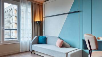 A modern room with a sofa, a chair, a lamp, and a window with curtains.