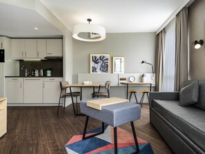 A modern kitchen with a built-in oven, a dining area with a table and chairs, a sofa, and a rug.