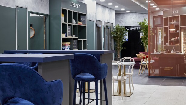 Een modern interieur met een bar, zitplaatsen, en afgebakende zones voor een bibliotheek en winkel.
