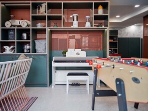 A room with a foosball table, a piano, a crib, and a shelf with various items. - Aparthotel Adagio Paris Suresnes Longchamp (Suresnes)