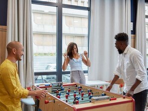 Ein Zimmer mit Kicker, großen Fenstern und Blick ins Freie.