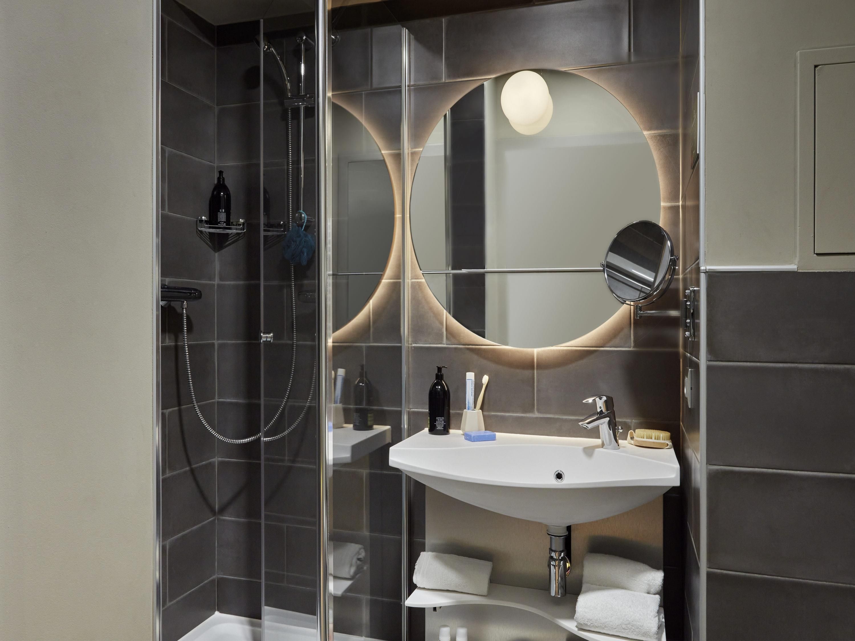 A modern bathroom with a glass-enclosed shower, a white sink, and a large mirror.