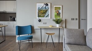 Un espace de vie moderne comprenant un canapé, un fauteuil bleu, une petite table avec une plante et deux tableaux encadrés accrochés au mur.