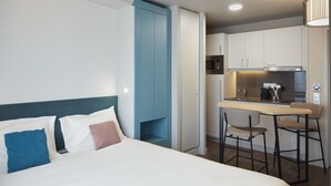 Een moderne hotelkamer met een bed, een kleine kitchenette en een eethoek met twee stoelen.