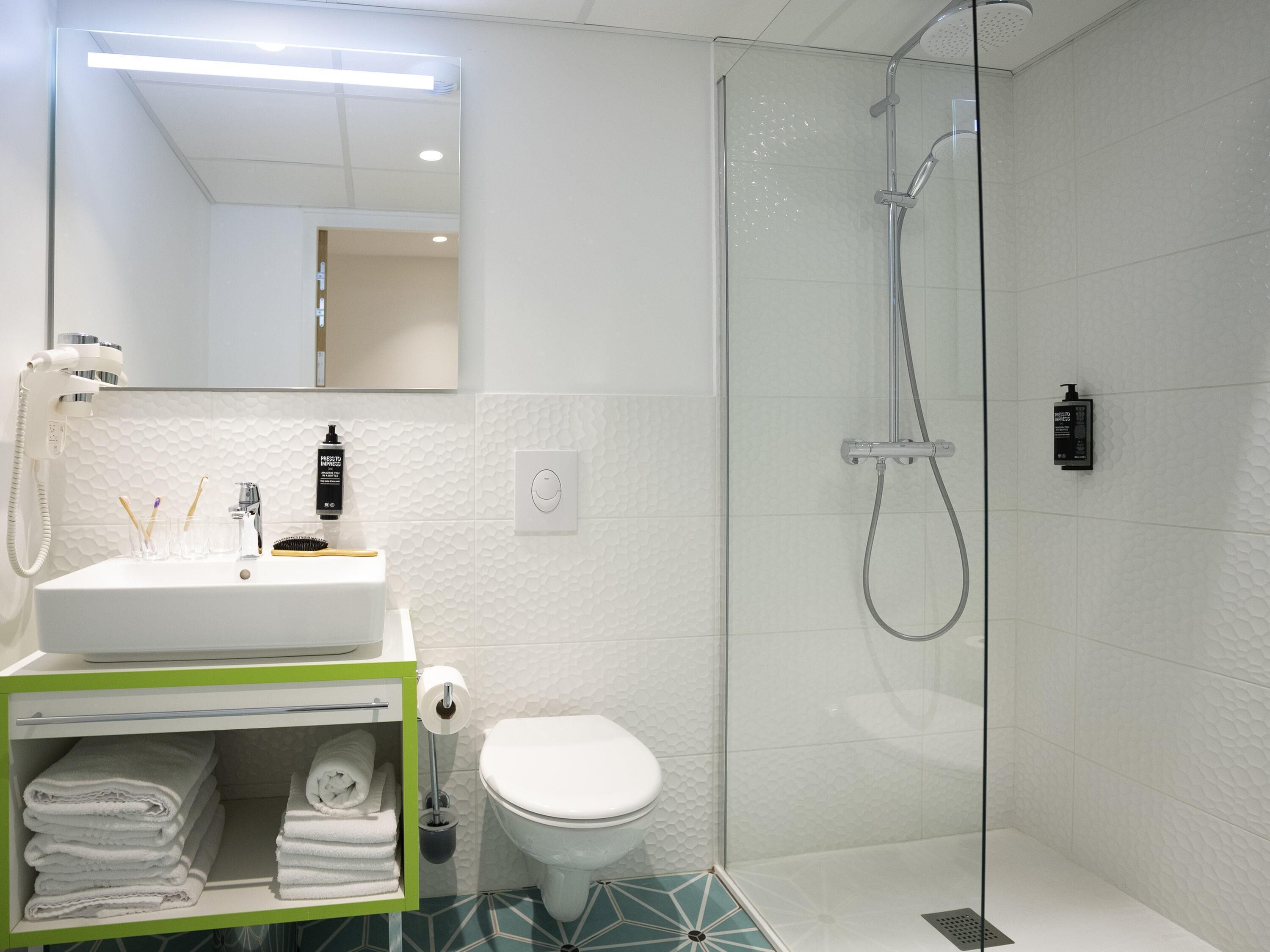 A modern bathroom with a glass-enclosed shower, a white sink with toiletries, and a toilet.