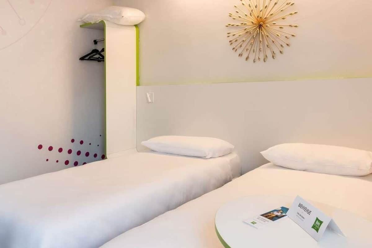 A hotel room with two beds, a decorative wall piece, and a small table with a brochure.