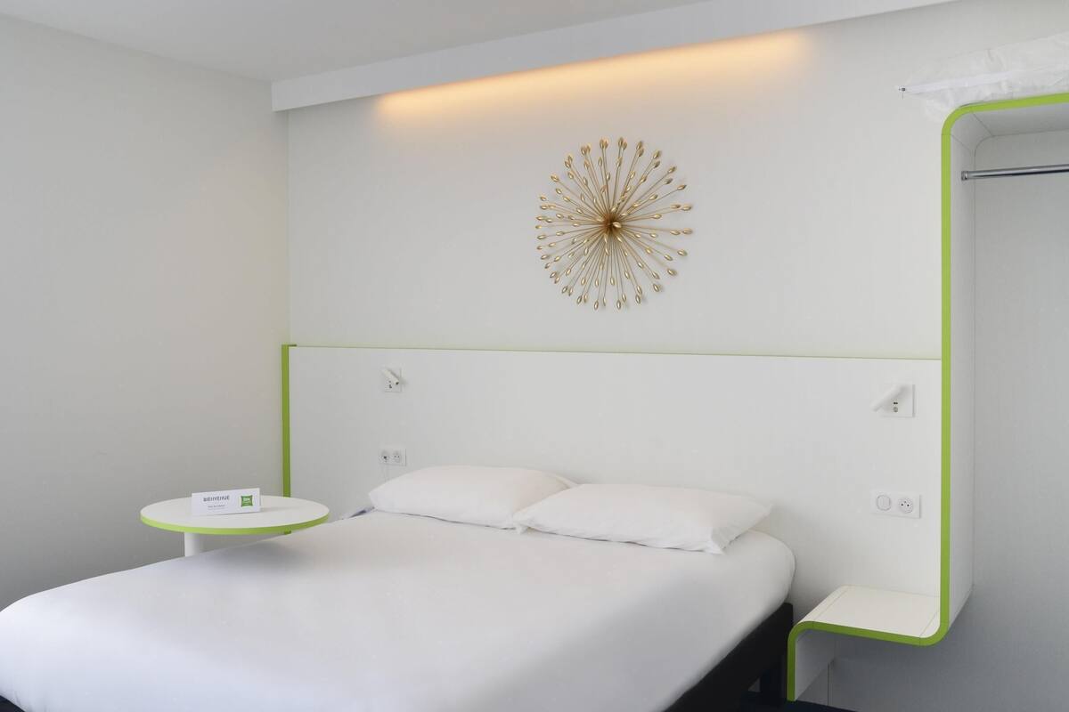 Una habitación de hotel moderna con cama, mesita de noche y un adorno en la pared.