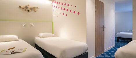 A hotel room with two beds, a blue polka dot carpet, a wall with pink dots, and a decorative light fixture.
