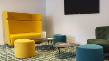 Una habitación con un sillón amarillo grande, un sillón verde azulado, una mesita redonda pequeña y un otoman verde.