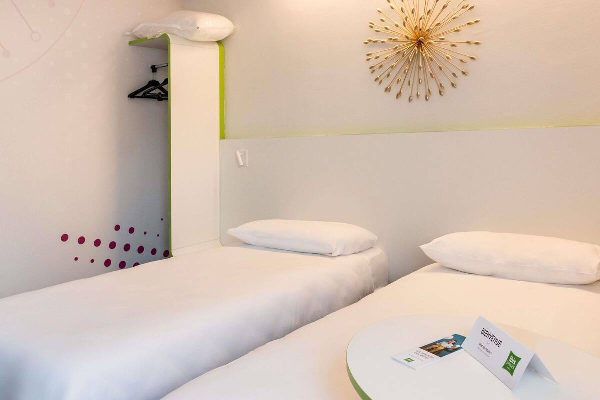 Habitación de hotel con dos camas, una lámpara de pared y una tarjeta de bienvenida sobre la cama.
