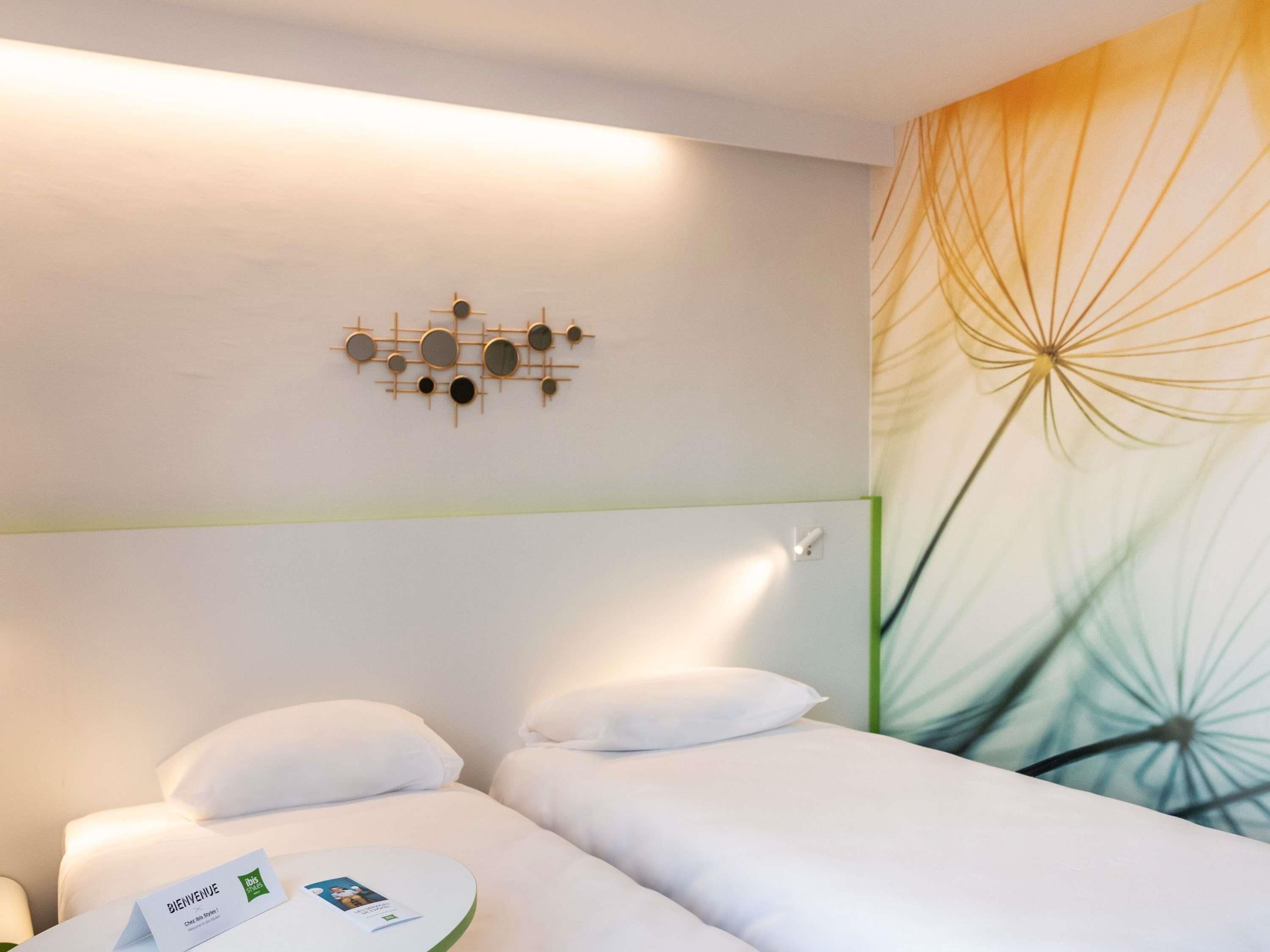 Une chambre d’hôtel comprenant un lit, un luminaire fixé au mur et un panneau décoratif mural.