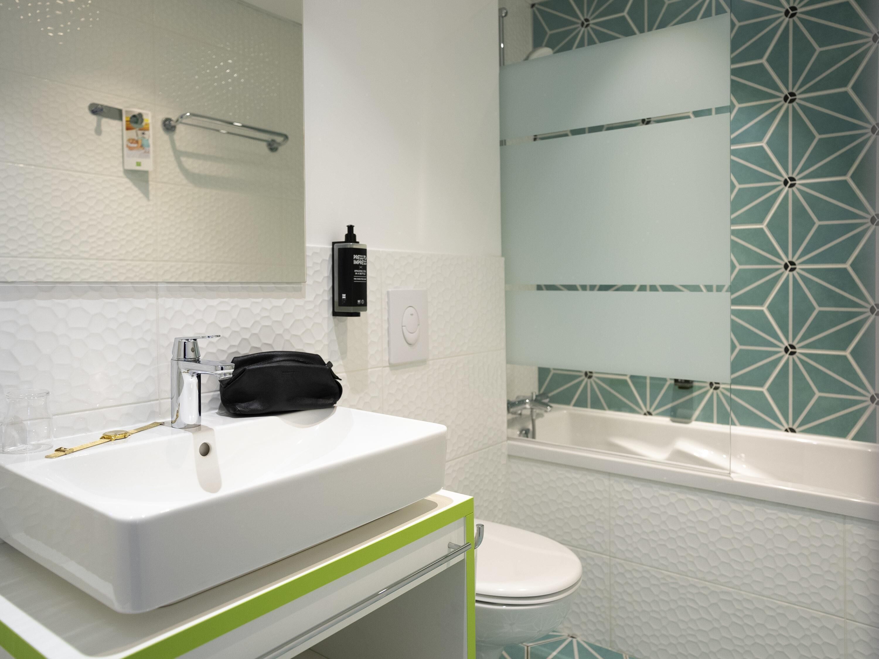 Un baño con un lavamanos blanco, un mueble de baño verde a rayas, un inodoro y una bañera.