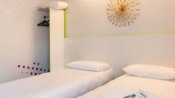 A hotel room with two beds, a wall-mounted light fixture, and a welcome card on the bed.