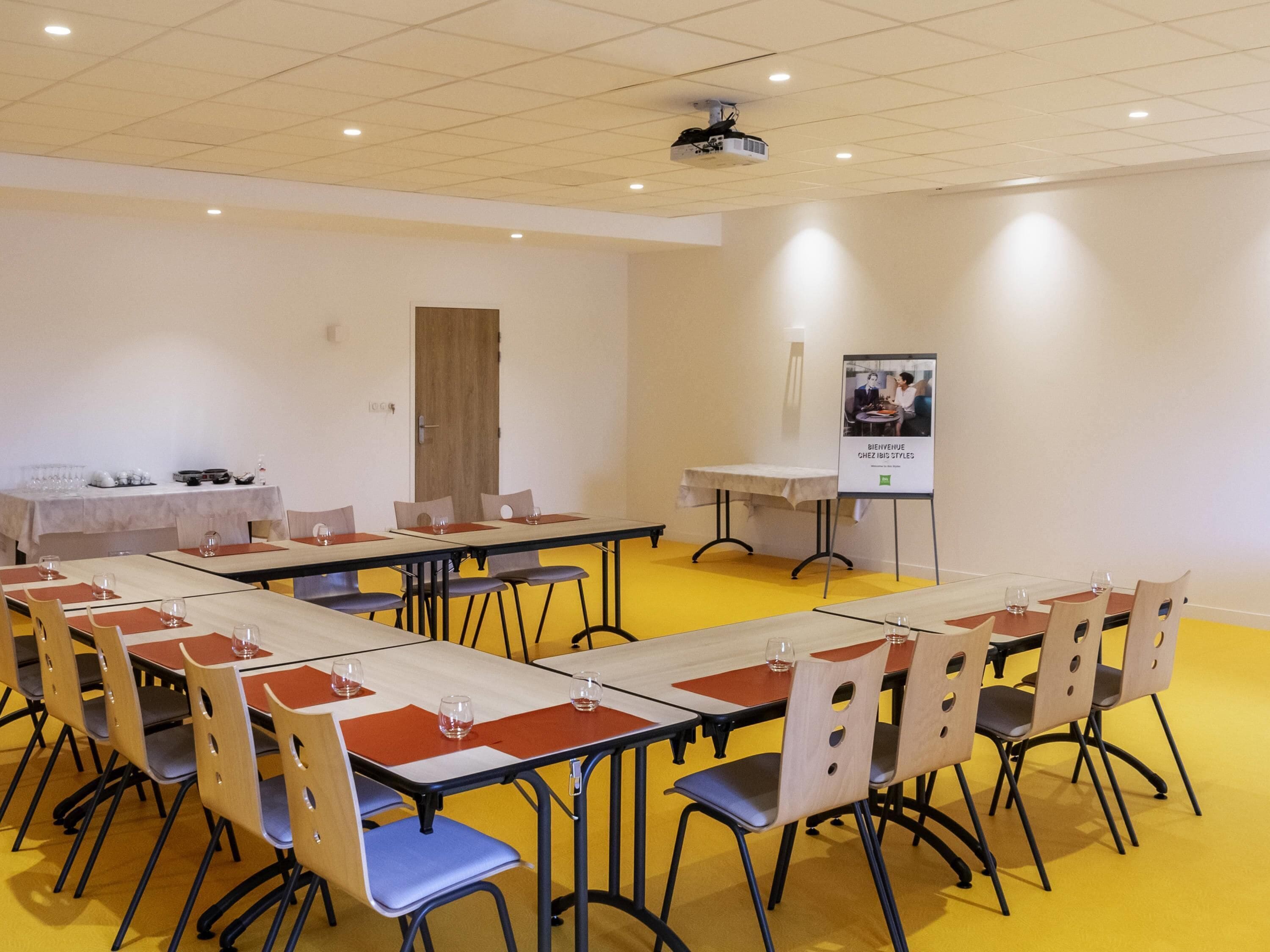 A conference room with tables and chairs, a projector, and a poster on the wall.