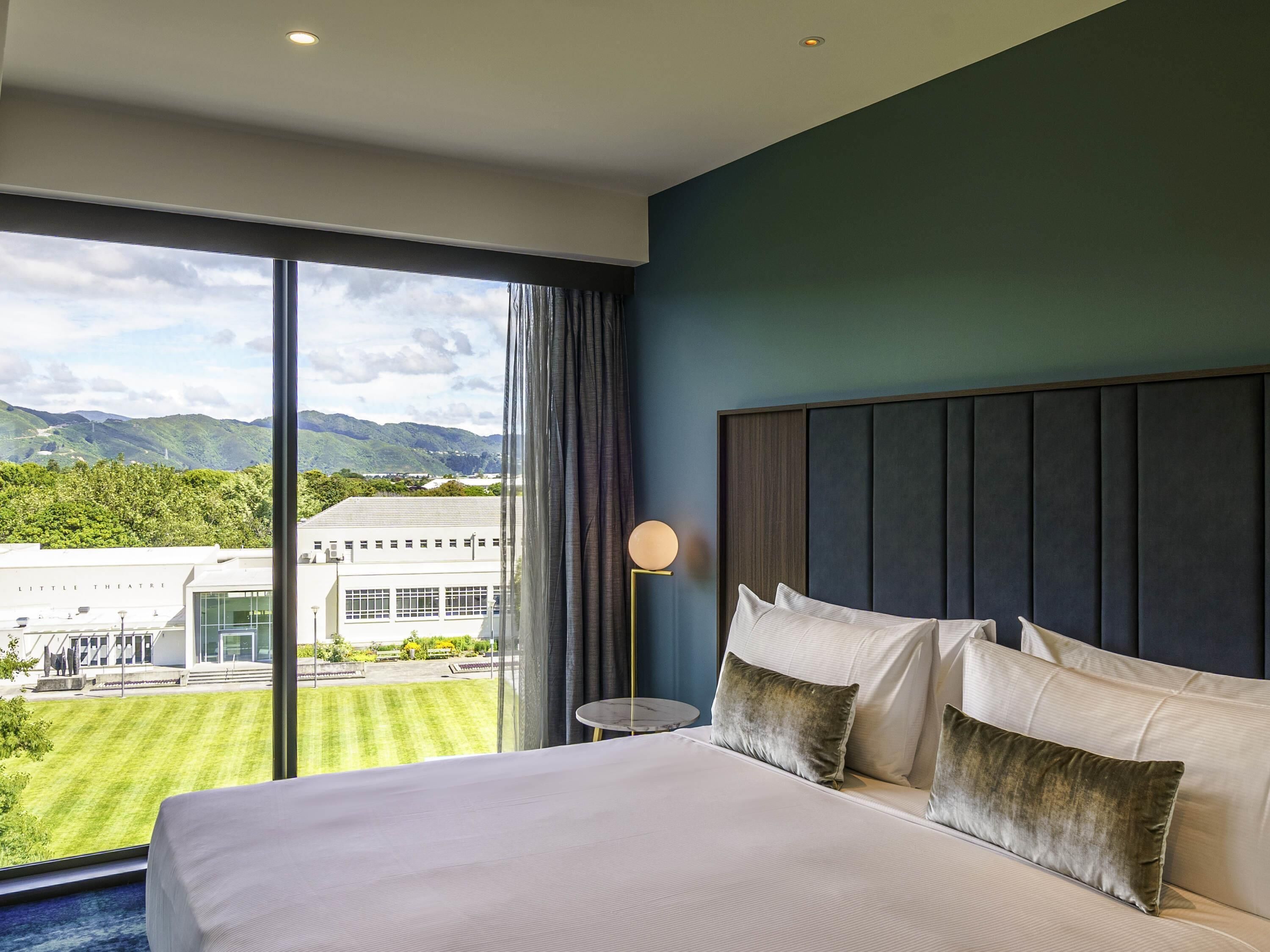 A hotel room with a large bed, a round table, and a view of a building and mountains.
