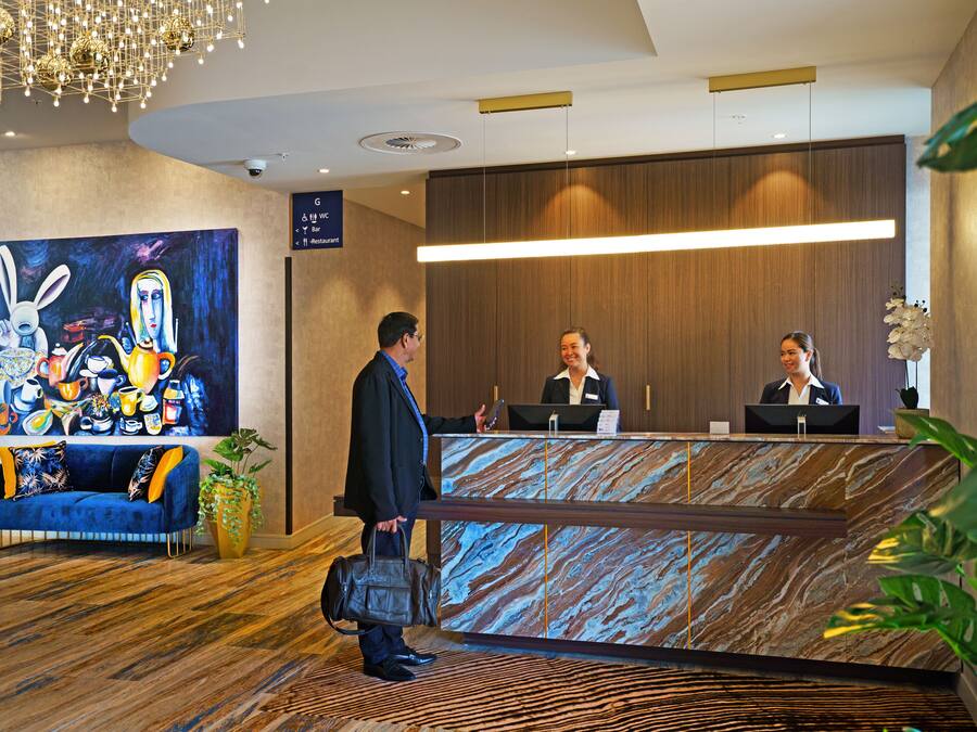 A hotel reception area with a marble reception desk, a large painting on the wall, and a blue sofa with orange cushions.