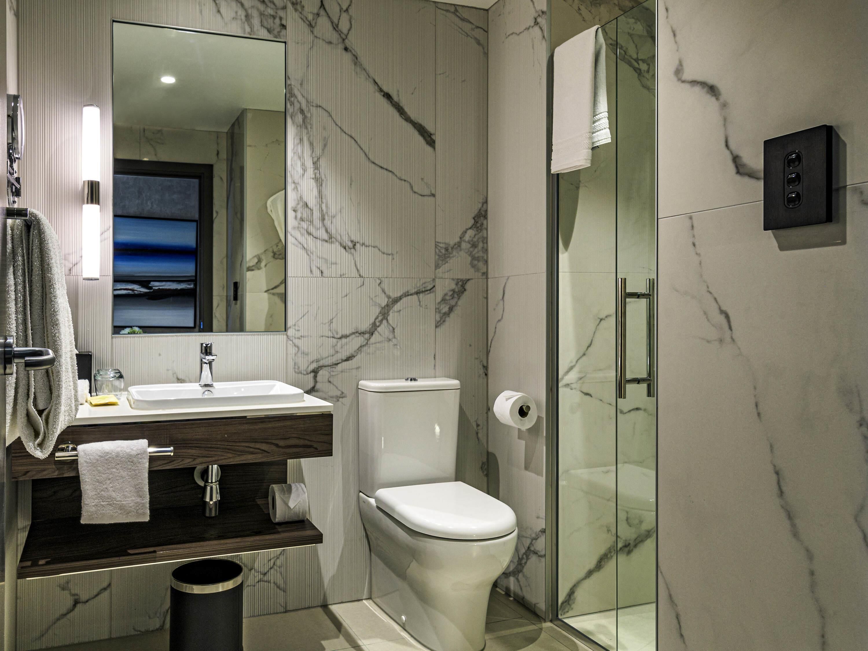 A modern bathroom with a marble wall, a glass shower enclosure, a toilet, and a sink with a mirror.