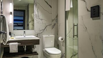 A modern bathroom with a marble wall, a glass shower enclosure, a toilet, and a sink with a mirror.