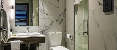 Un baño moderno con pared de mármol, cabina de ducha de cristal, inodoro y lavamanos con espejo.