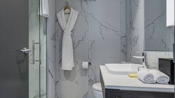 Un bagno moderno con box doccia in vetro, parete in marmo, lavabo bianco e mobile vanitario in legno scuro.