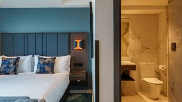 Een hotelkamer met een bed, nachtkastje, lamp en een badkamer met toilet en marmeren wanden.