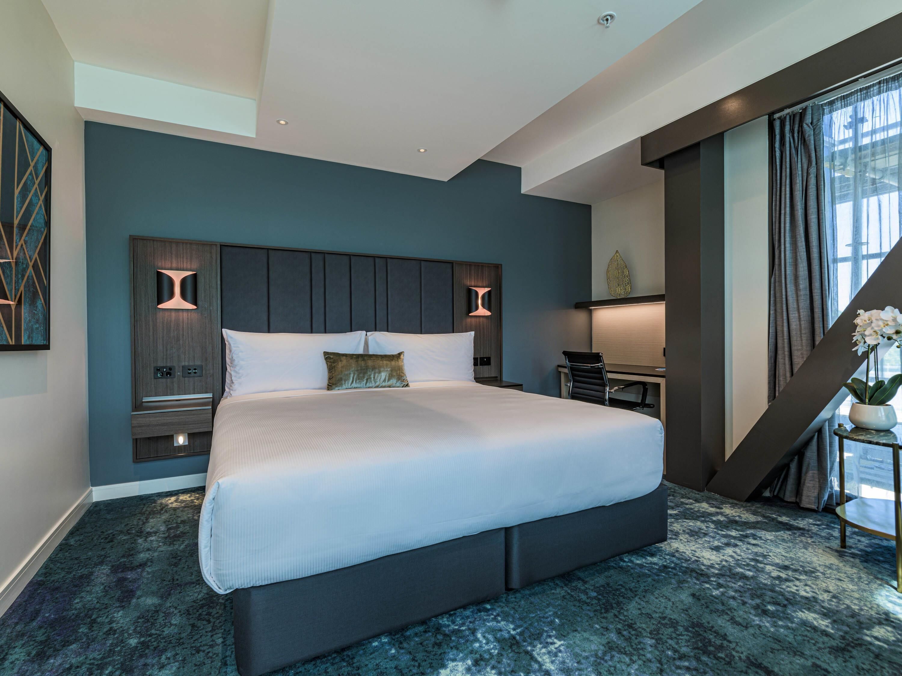 A modern hotel room with a large bed, a desk, and a chair.