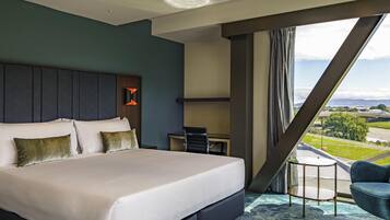 A modern hotel room with a large bed, a desk, and a view of the city.