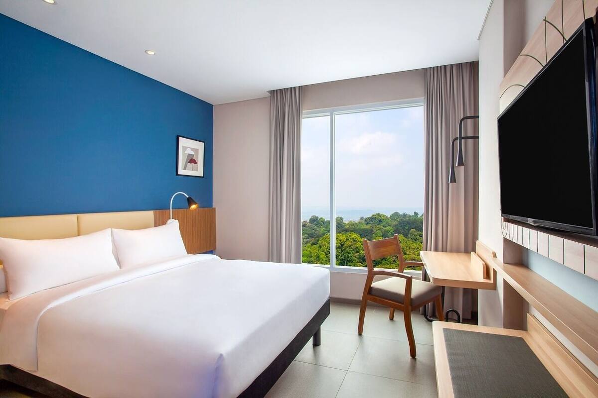 A hotel room with a large bed, a desk, a TV, and a view of the outdoors.