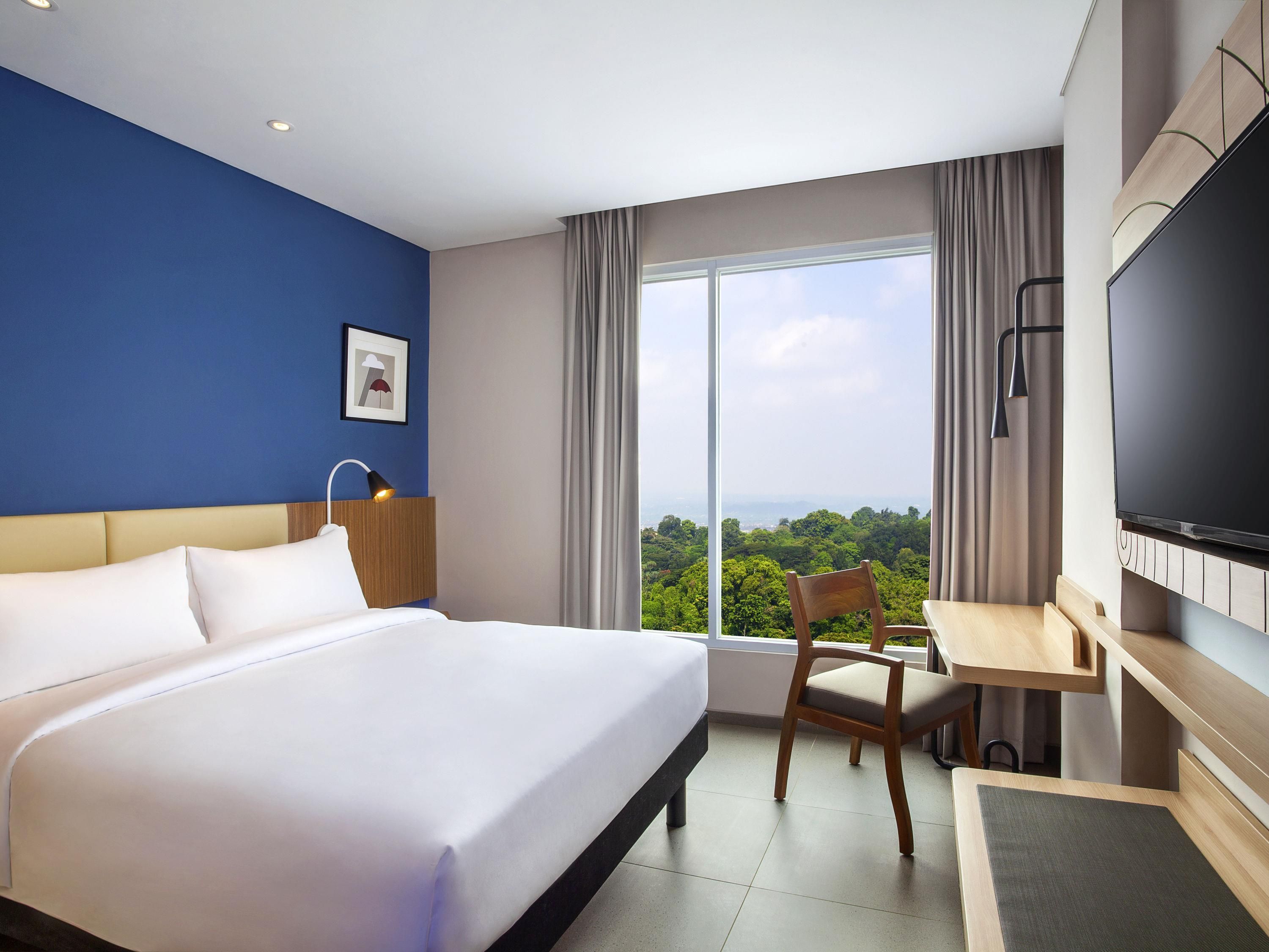 A hotel room with a bed, a desk, a chair, a TV, and a large window with a view.