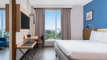 Une chambre d’hôtel comprenant un lit, un bureau avec une chaise, une télévision, une fenêtre avec des rideaux et une vue sur la ville.