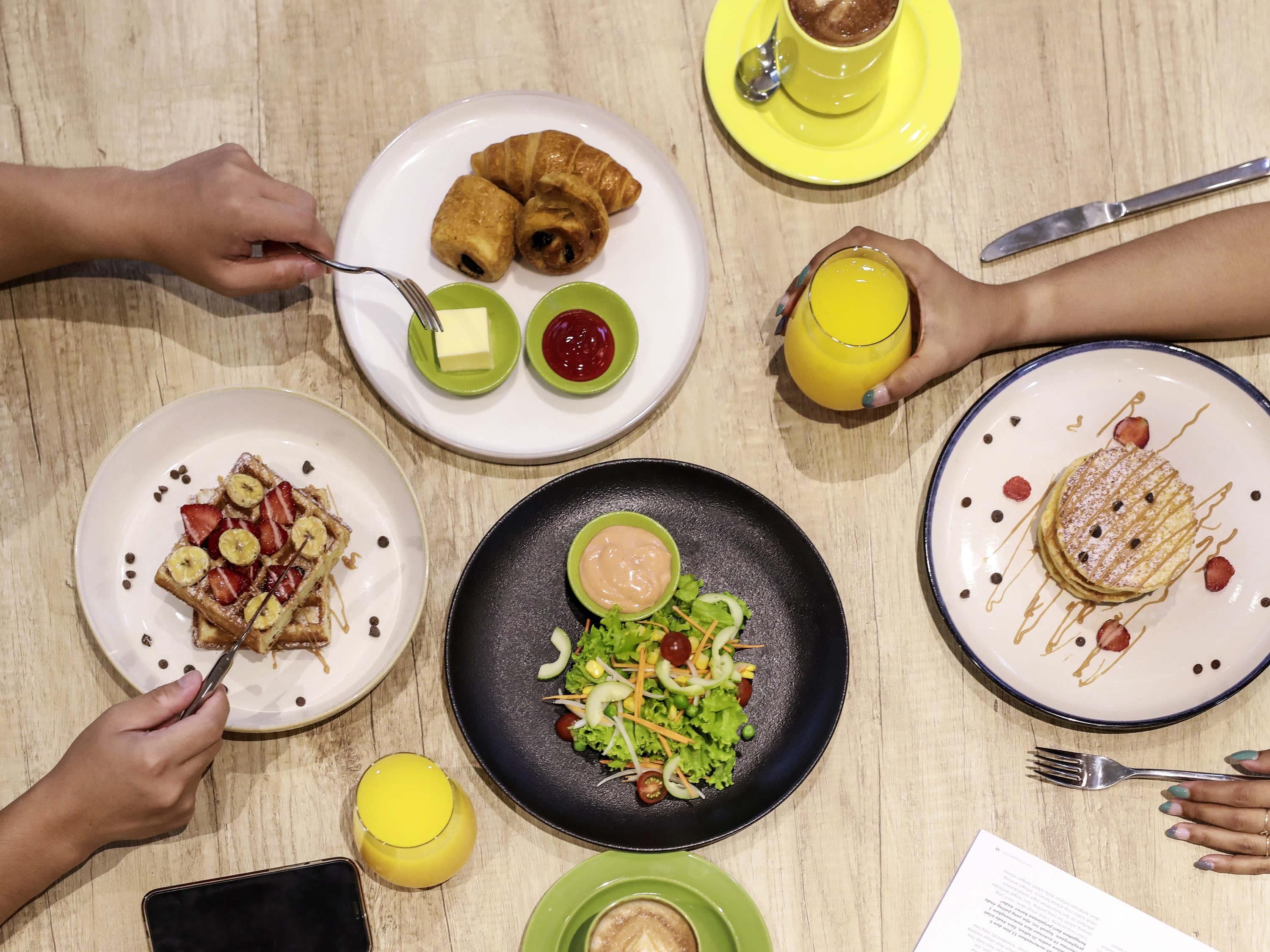 Una mesa con diversos alimentos para el desayuno, como cruasanes, gofres y una ensalada.