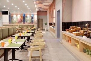 Un restaurante moderno con mesas comunitarias largas y cabinas, una barra de cocina con productos alimenticios y un colorido diseño de techo.