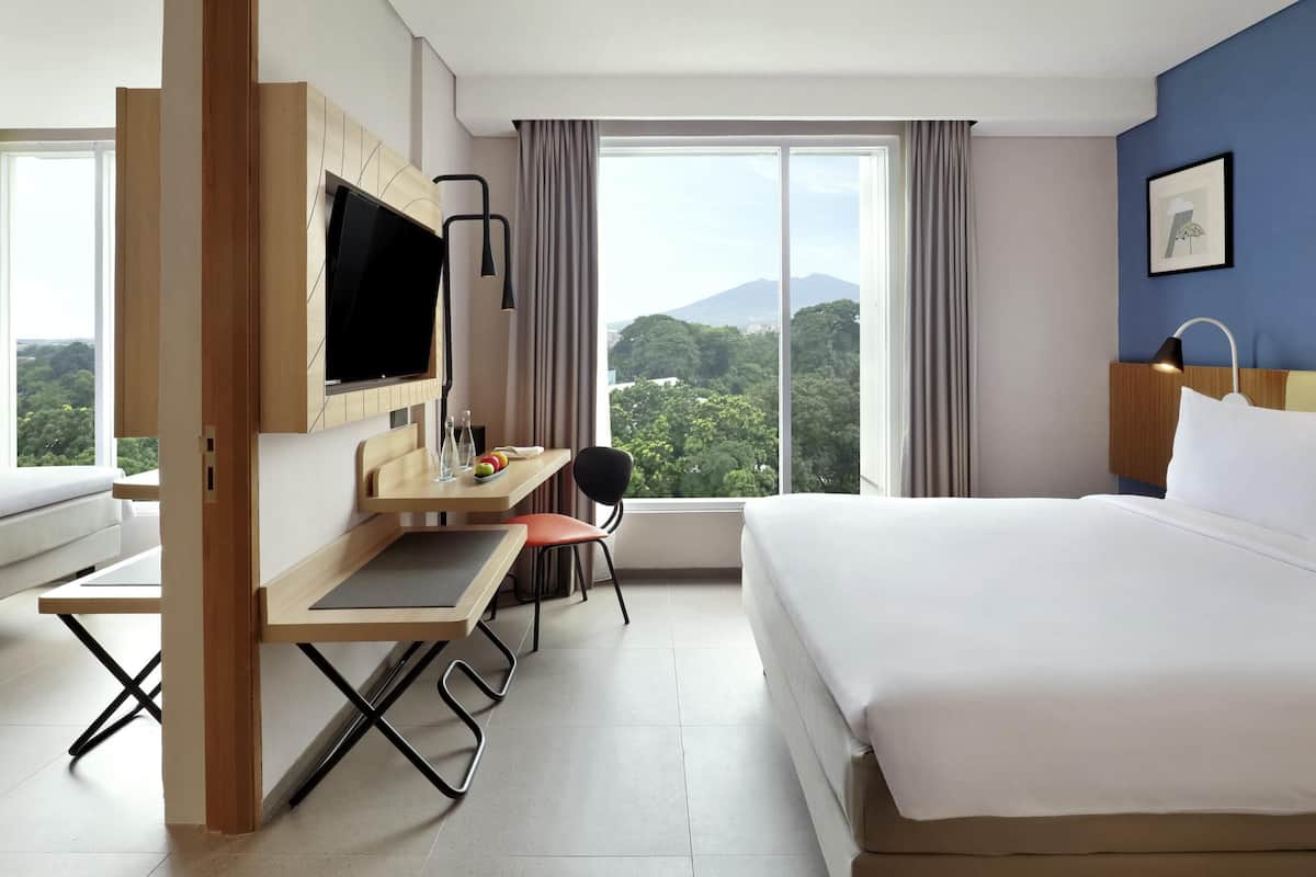 A hotel room with a bed, a desk with a chair, a TV, and a large window with a mountain view.