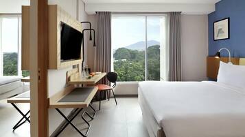 A hotel room with a bed, a desk with a chair, a TV, and a large window with a mountain view.