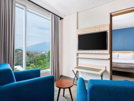 Habitación de hotel con un ventanal grande, un televisor de pantalla plana montado en la pared, una cama y dos sillones azules.