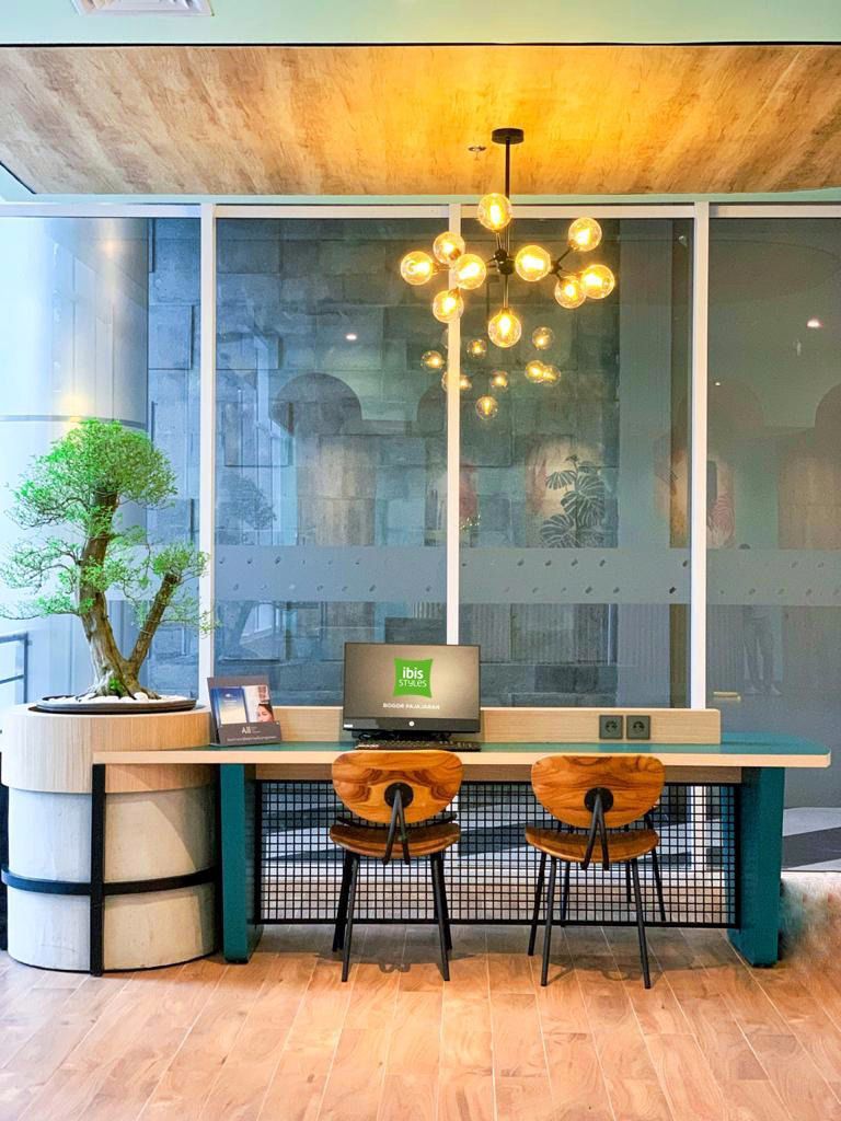 Een moderne werkruimte met een houten bureau, twee stoelen, een potplant en een hanglamp.