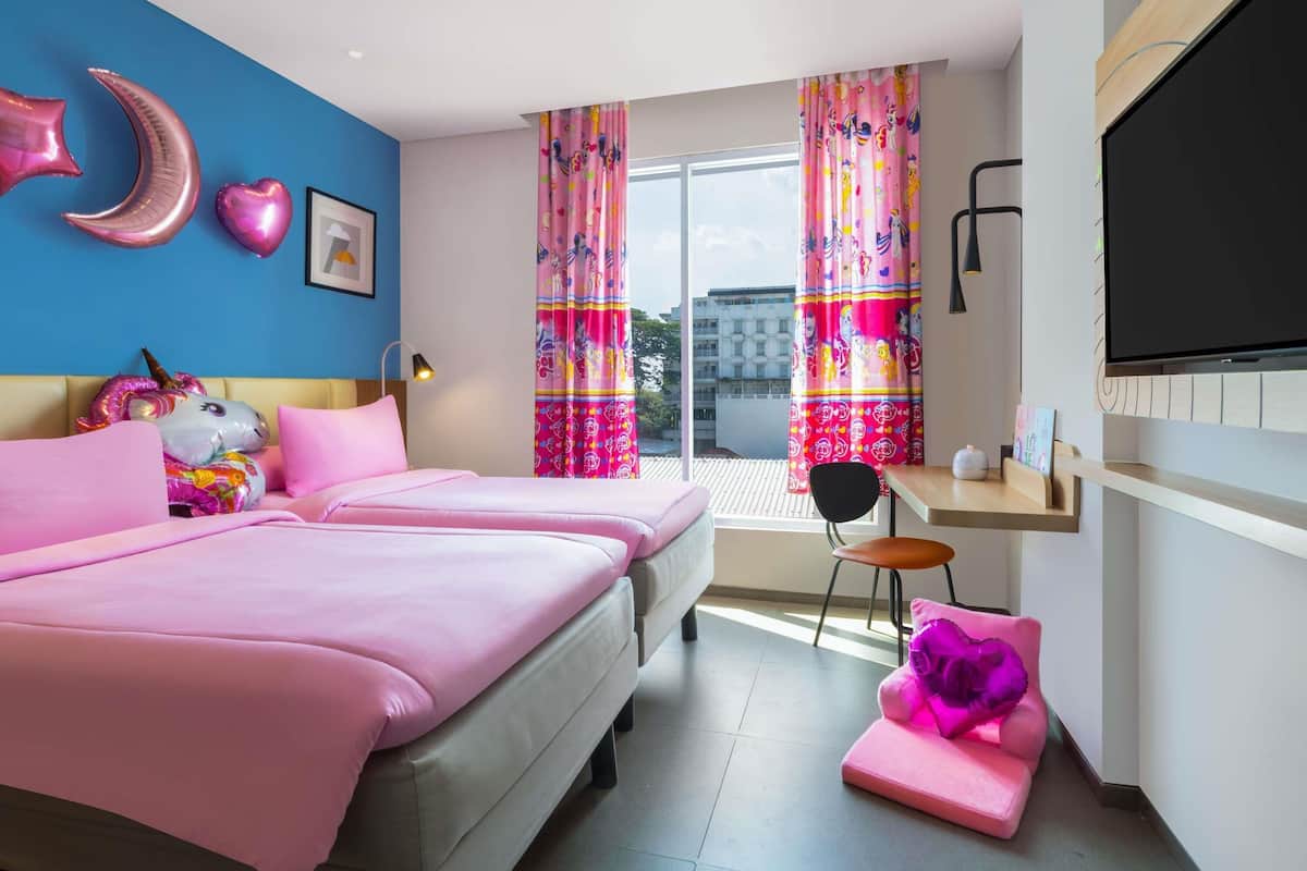 A bedroom with two beds, a desk, a TV, and colorful curtains.