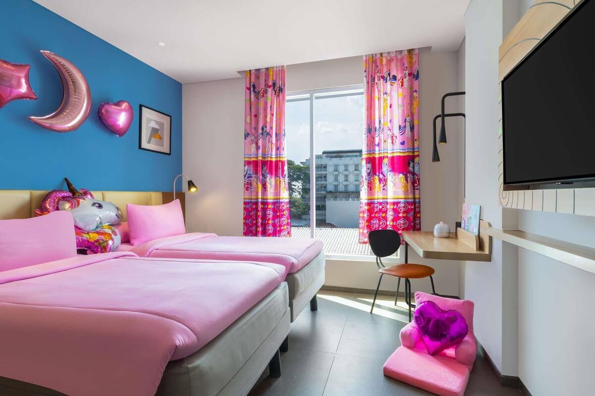 A bedroom with two beds, a TV, a desk, and a window with curtains.