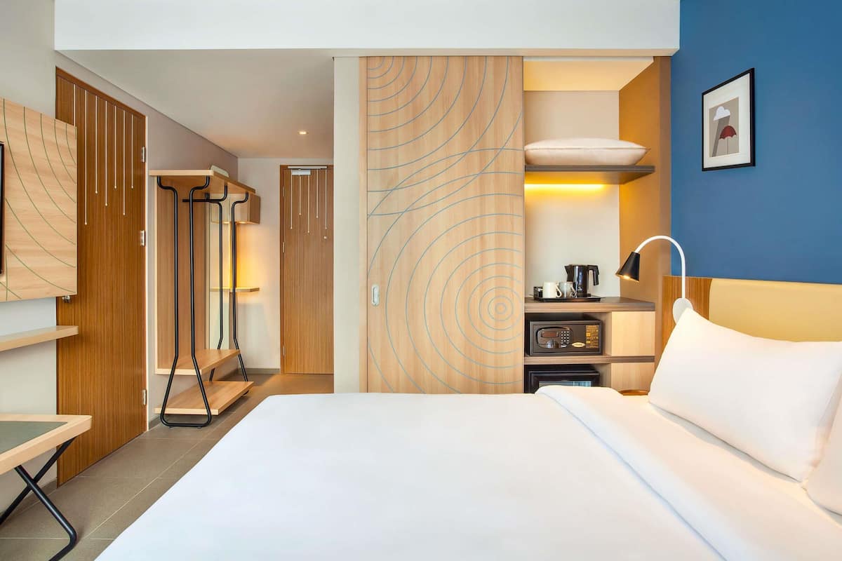 A hotel room with a bed, a desk, a microwave, a coffee maker, and a wardrobe.