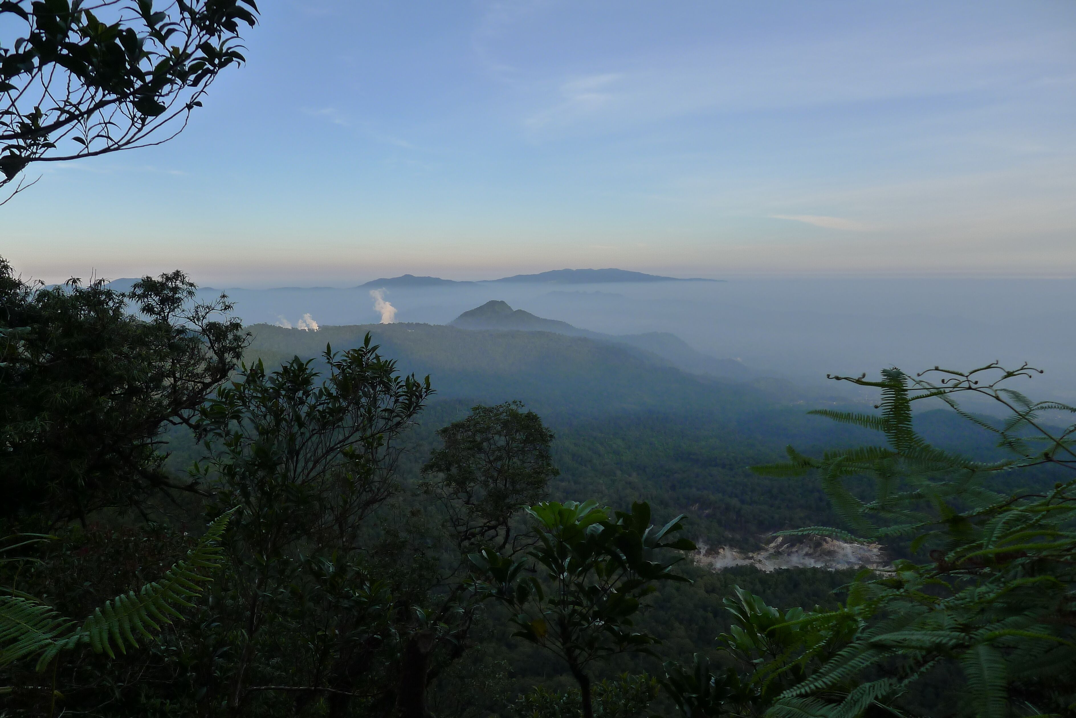 A mountainous landscape with dense forest and a visible smoke plume.