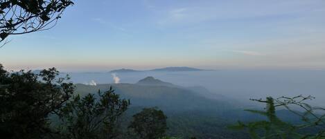 A mountainous landscape with dense forest and a visible smoke plume.