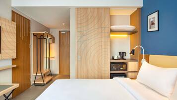 Quarto de hotel com cama, escrivaninha, micro-ondas, cafeteira e guarda-roupa.