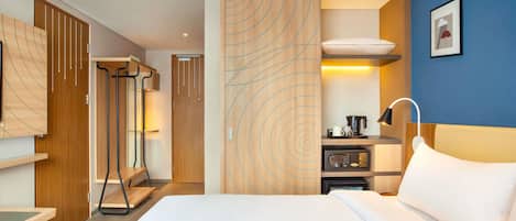 Une chambre d’hôtel équipée d’un lit, d’un bureau, d’un four à micro-ondes, d’une machine à café et d’une armoire.