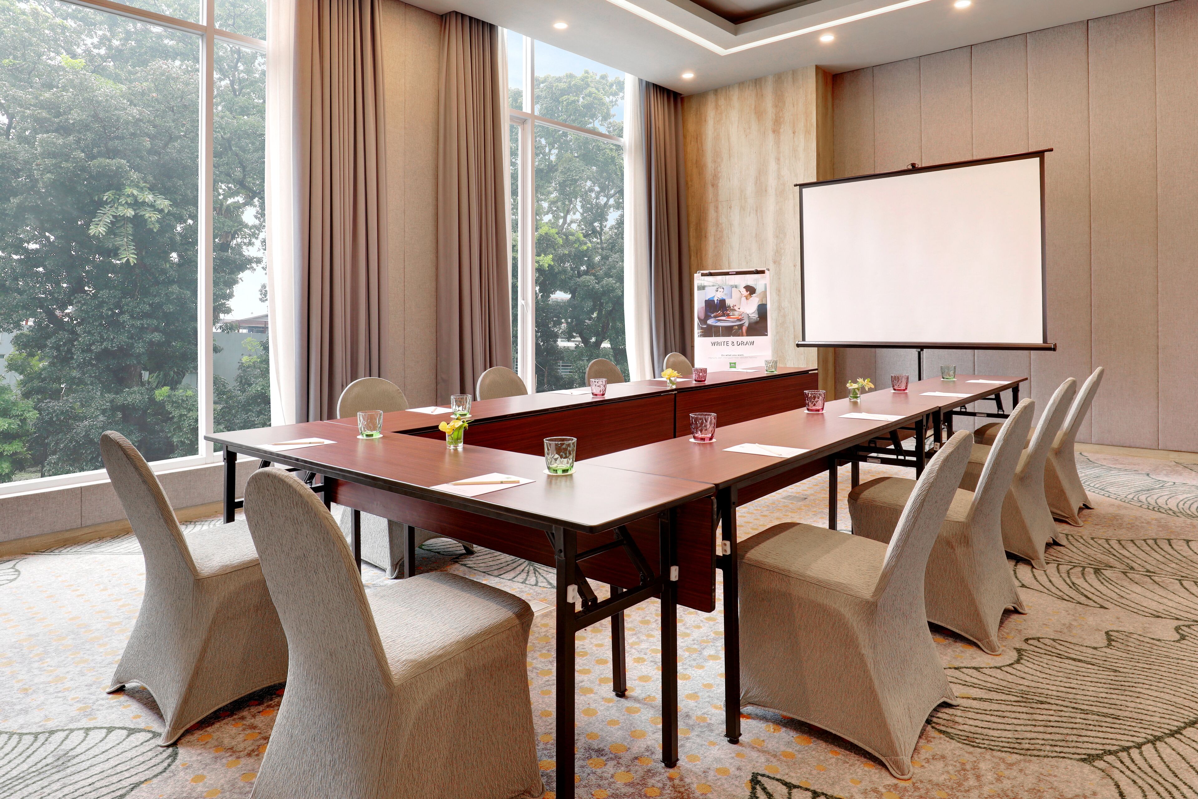 A conference room with a long table, chairs, a projector screen, and a poster.