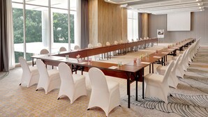 A conference room with a long table, white chairs, and large windows. - ibis Styles Bogor Pajajaran (Bogor)